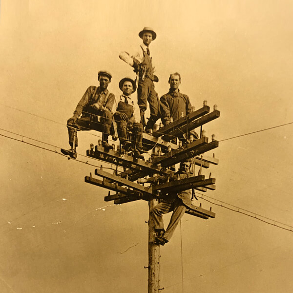 historical photo of men standing on the top of a telephone pole